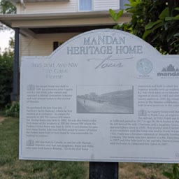 A weathered Heritage Home sign for the Cass Home with the house behind it
