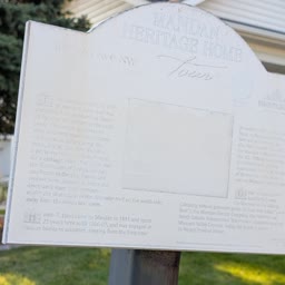 A faded Heritage Home sign for the Lyon-Weigel Home with the house behind it