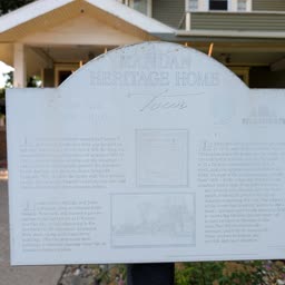 A faded Heritage Home sign for the McGillic Home with the house behind it